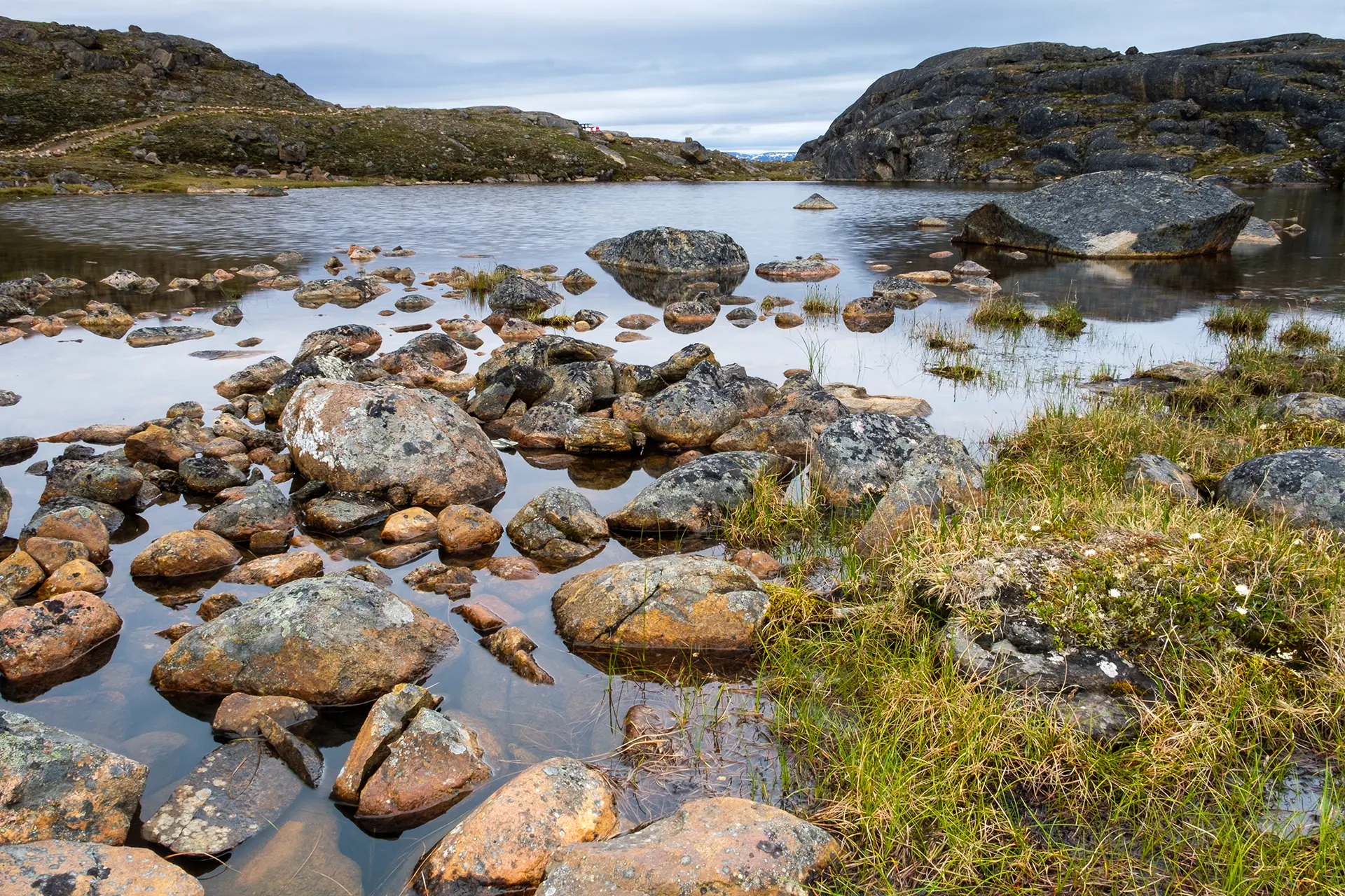Nunavut landscape - rocks next to a small lake with mountains at the background