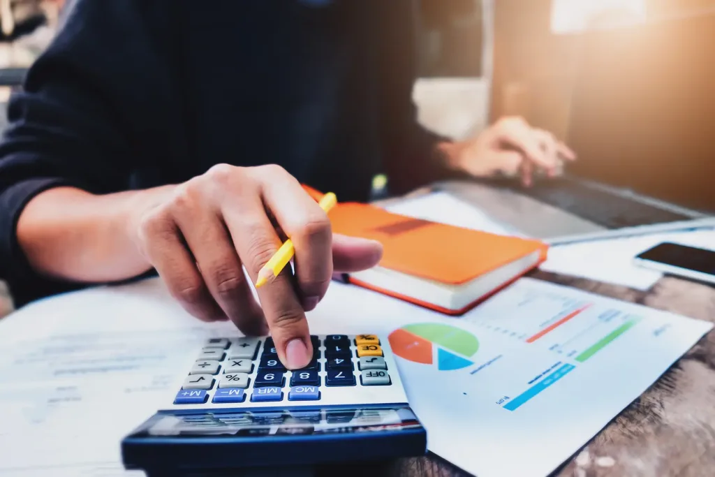 man holding pen using calculator and laptop computer to analysys calculate financial & budget & tax data document with notebook in working on wood desk in office