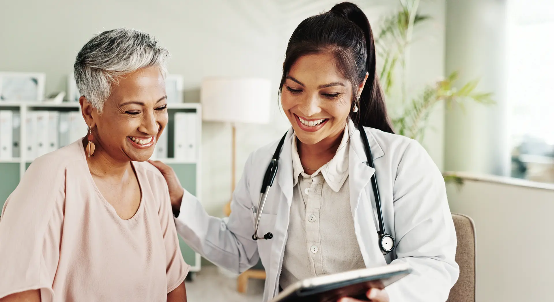 Smile, doctor and senior patient on tablet in office for good news, research and online results of diagnosis.